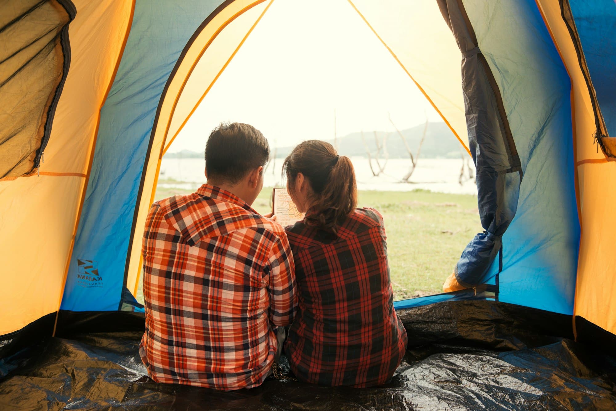 young backpackers sitting in a tent looking at book and planning their next camping adventure.